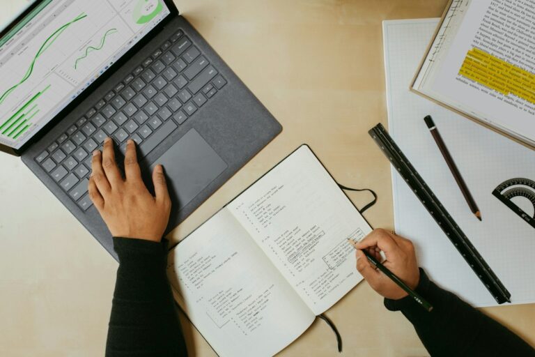 Person writing a bi-weekly vs monthly budget in a notebook at a kitchen table
